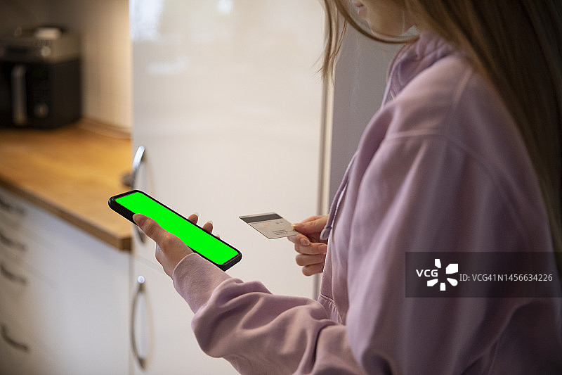 少女在厨房用信用卡在手机上进行网购图片素材