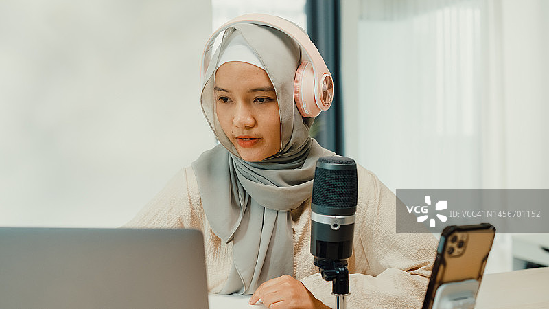 快乐的穆斯林亚洲女孩戴着头巾，在工作室房间里检查并准备乐器，在笔记本电脑和麦克风上录制播客，进行直播图片素材