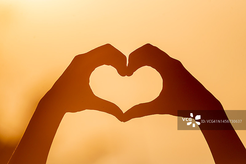 年轻人手牵手组成心形，橙色逆光剪影图片素材
