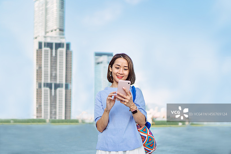 在市中心通勤时愉快地使用智能手机的年轻漂亮亚洲女人图片素材