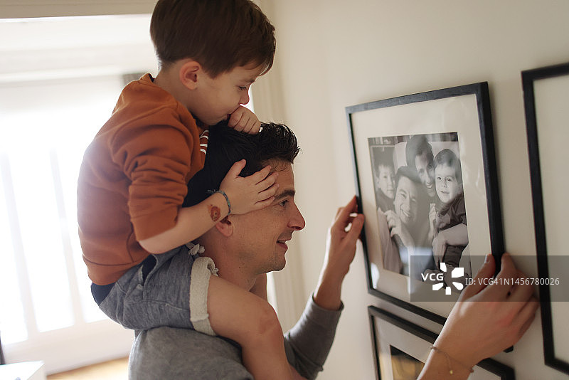 爸爸在墙上挂画框，儿子骑在他的肩膀上图片素材