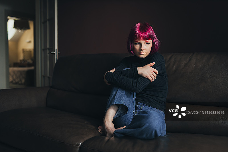 不开心的紫发年轻女子坐在家里的沙发上图片素材