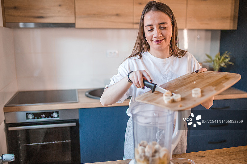 微笑的女运动员将切碎的香蕉放入搅拌机图片素材