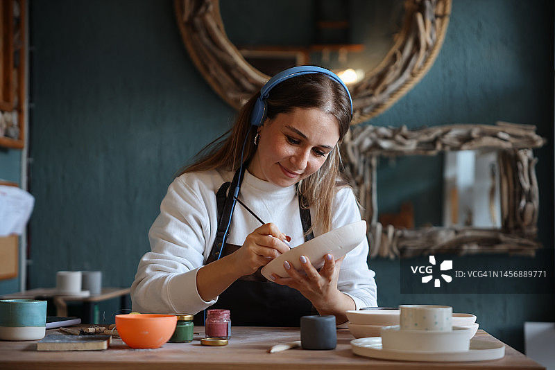 身穿围裙的年轻女子在工作室绘画陶器图片素材