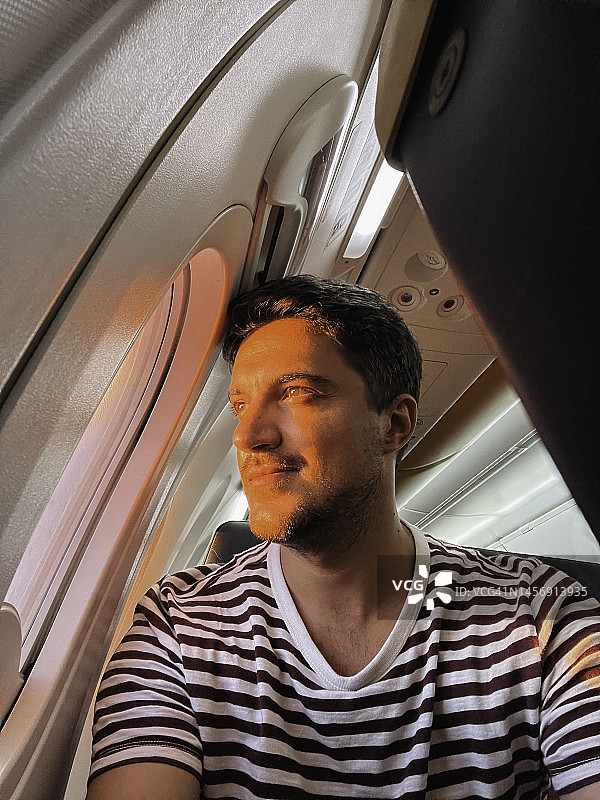 日落时分，在飞机上看着窗外的年轻男人图片素材