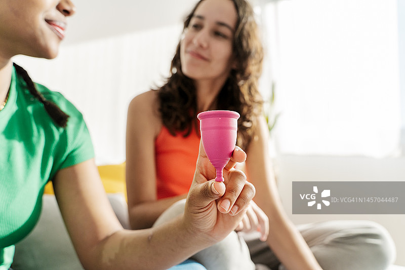年轻女人向朋友讲解月经杯的工作原理，月经和月经杯概念图片素材