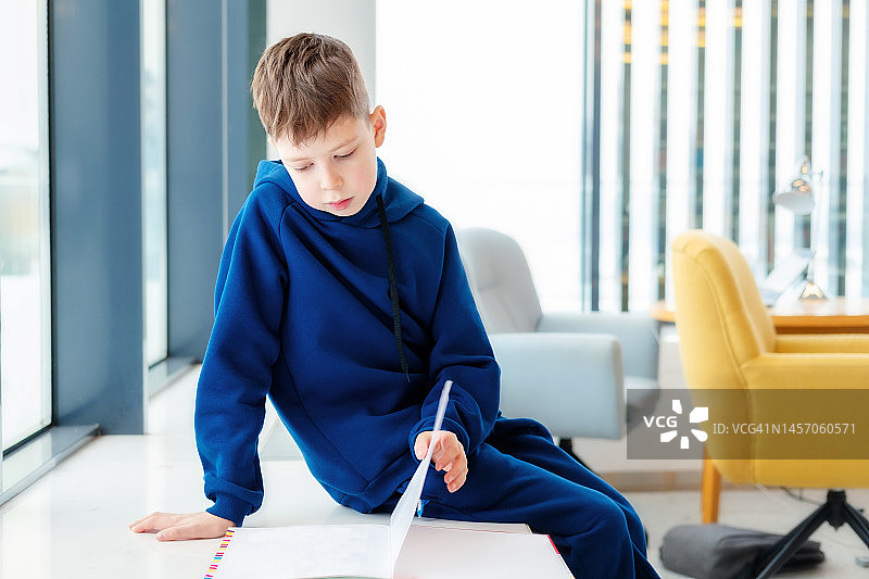 穿着蓝色连帽衫的男学生坐在图书馆的窗台上读书图片素材