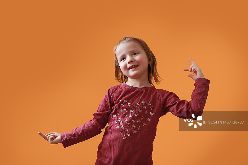 在橙色背景上跳舞的有趣小女孩图片素材