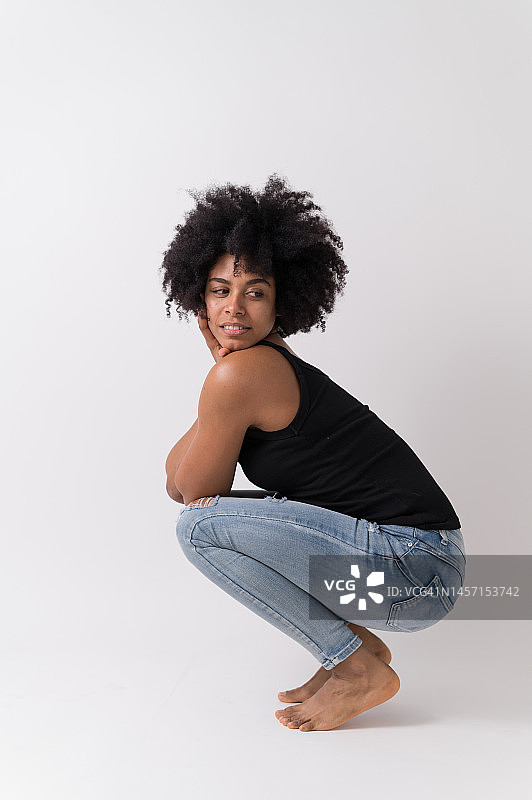 年轻女子在白色背景下蹲着，留着非洲发型的工作室肖像图片素材