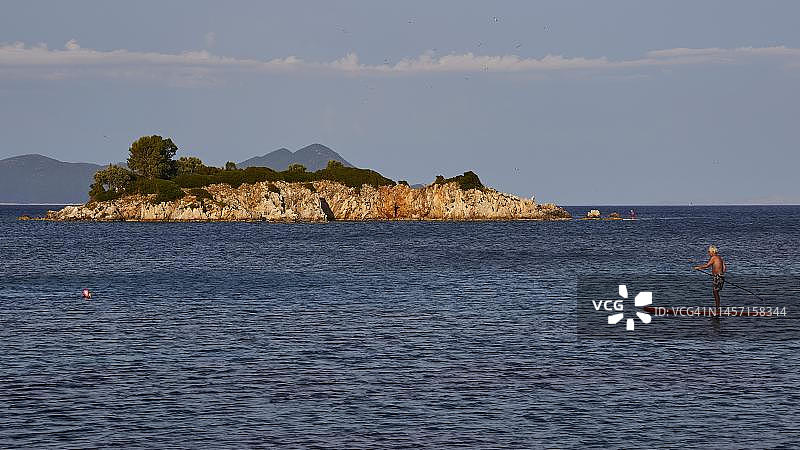 希腊伊萨卡岛爱奥尼亚群岛阿吉奥斯·尼古拉斯岛马尔马卡斯湾站立式桨板和蓝色天空图片素材