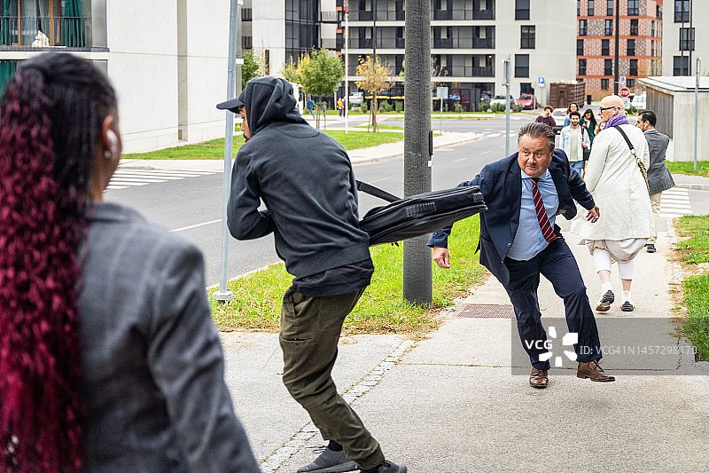 戴帽衫的小偷在街上偷中年男人的包图片素材