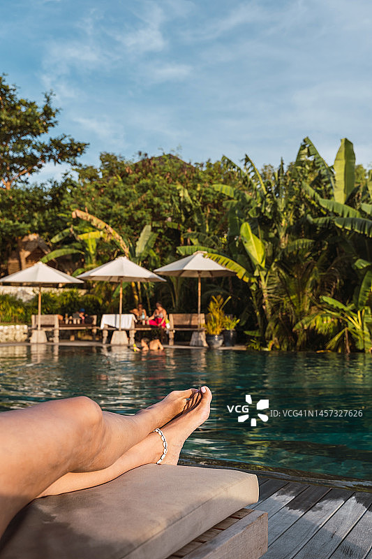 在热带度假胜地的无边泳池边，棕榈树背景下，女人在享受日光浴图片素材