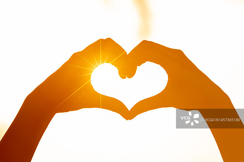 年轻人手牵手组成心形，橙色逆光剪影图片素材