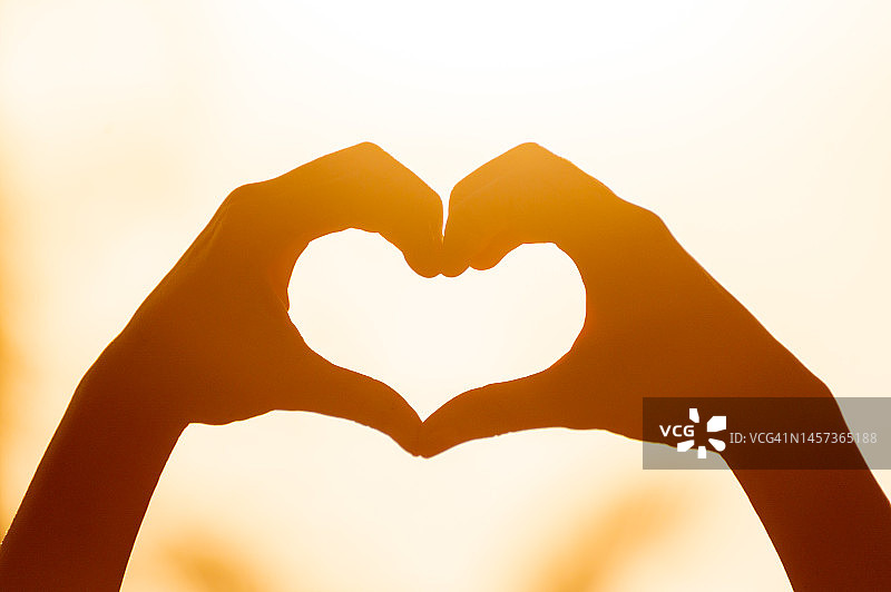 年轻人手牵手组成心形，橙色逆光剪影图片素材