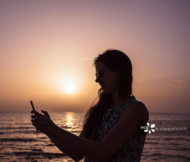 夏季假期中自拍日落的女人（竖版照片）图片素材