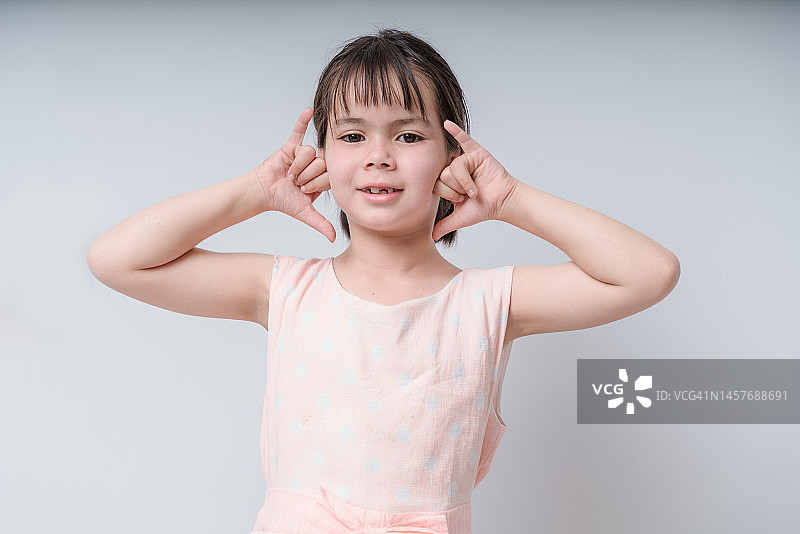 微笑的亚洲小女孩在白色背景上手势示意打电话图片素材