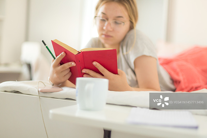 少女在卧室的床上看书，桌子上放着一杯咖啡图片素材