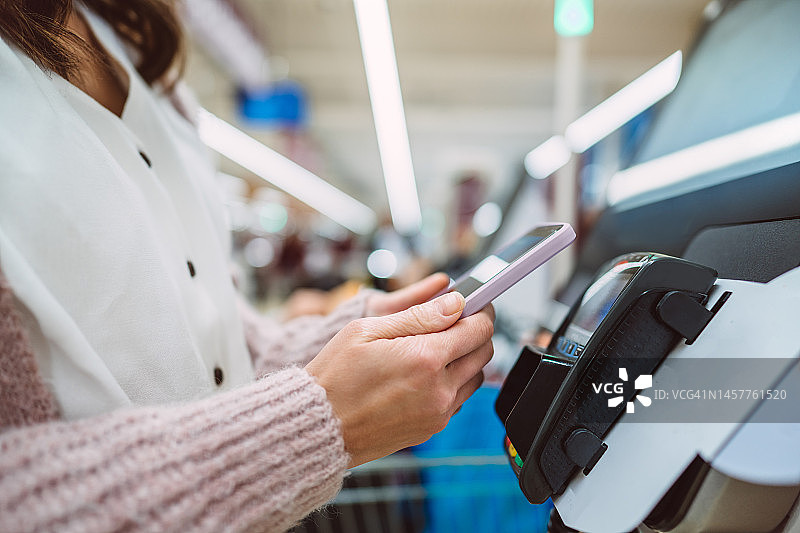 女顾客在超市自助结账时使用手机进行非接触式支付图片素材