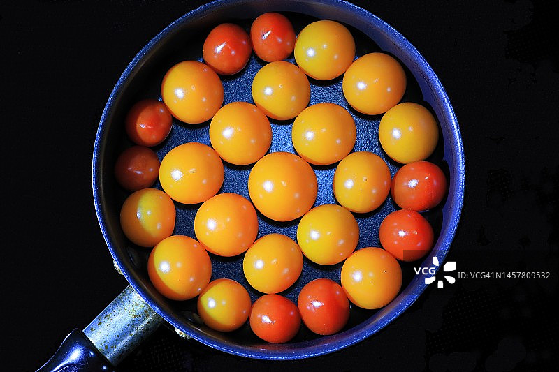 黑色背景煎锅中的红黄橙迷你小番茄图片素材