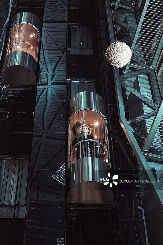 乘坐透明电梯上到高层的年轻女人，未来主义概念，时尚服装和发型，带有复制空间的球形太空球模型图片素材