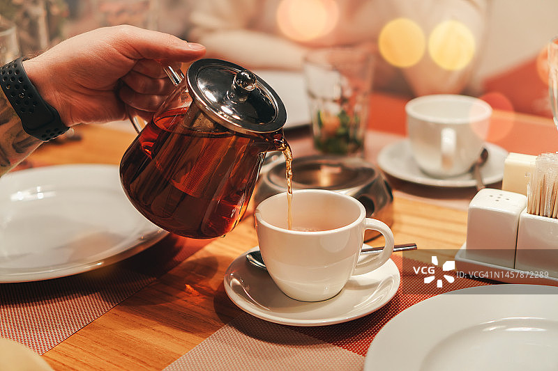 在舒适的茶馆里，男人将红茶倒入白色陶瓷杯中图片素材