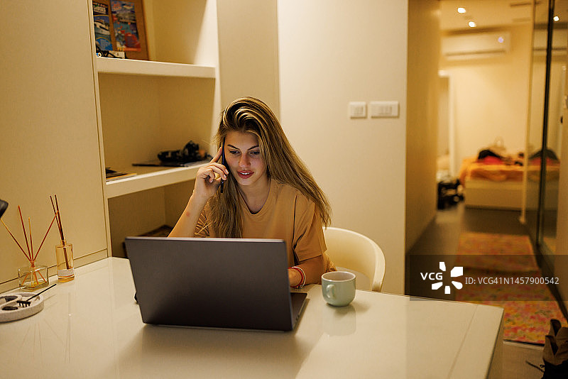 晚上在家使用笔记本电脑打电话的年轻女子图片素材