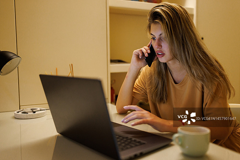 晚上在家使用笔记本电脑打电话的年轻女子图片素材