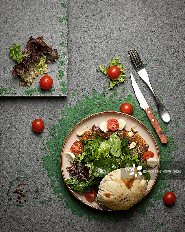 皮塔饼，内馅为菠菜、生菜、番茄、肉和鹌鹑蛋，餐盘上配有刀叉。深色背景。俯视图。餐具。东方美食图片素材
