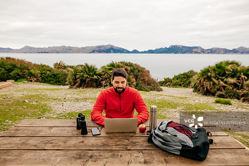 年轻徒步者在马略卡岛北部海岸波连萨湾的露营地使用笔记本电脑工作图片素材