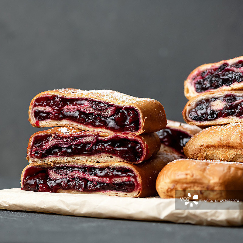 纸上的切块樱桃馅卷，水果馅甜点，深色背景，特写图片素材
