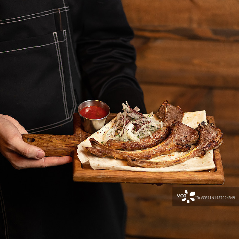烤羊排配皮塔饼、红酱和腌洋葱，厨师手持木板，餐厅菜单美食，柔焦俯视图片素材