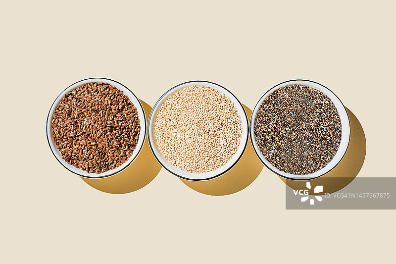 种子拼盘，健康食品配料，超级食品。平铺，俯视图，复制空间。奇亚籽，亚麻籽，米色背景上的白芝麻籽。图片素材