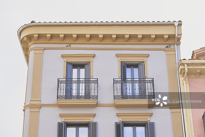 具有古典设计的白色和黄色建筑，有希腊式柱子，阳台和带有蓝色木制百叶窗的窗户图片素材