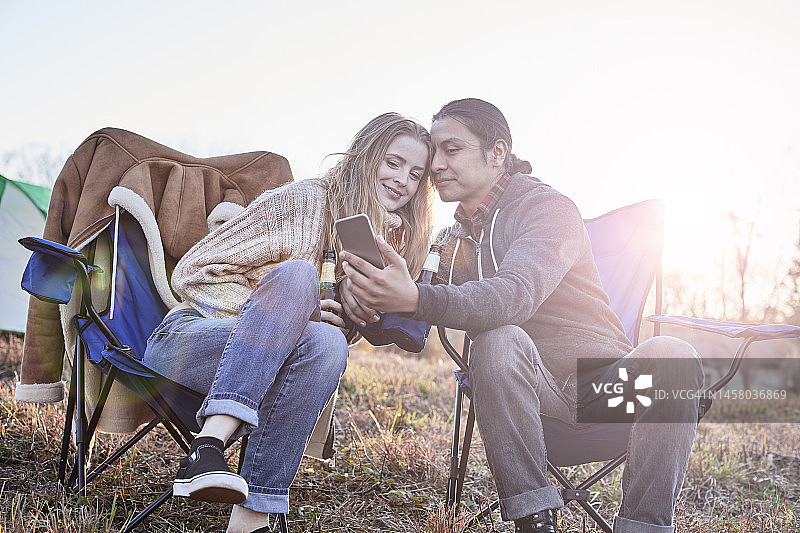 坐在露营椅上喝啤酒的西班牙裔男子和金发白人女子图片素材