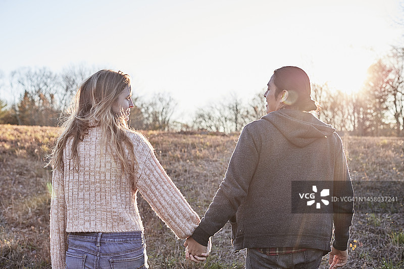日落时分，西班牙裔男子和金发白人女子手牵手散步图片素材