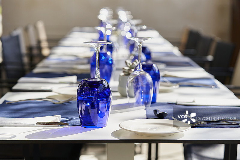 为庆祝活动准备的大型餐厅，蓝色酒杯成排摆放，正面视角图片素材