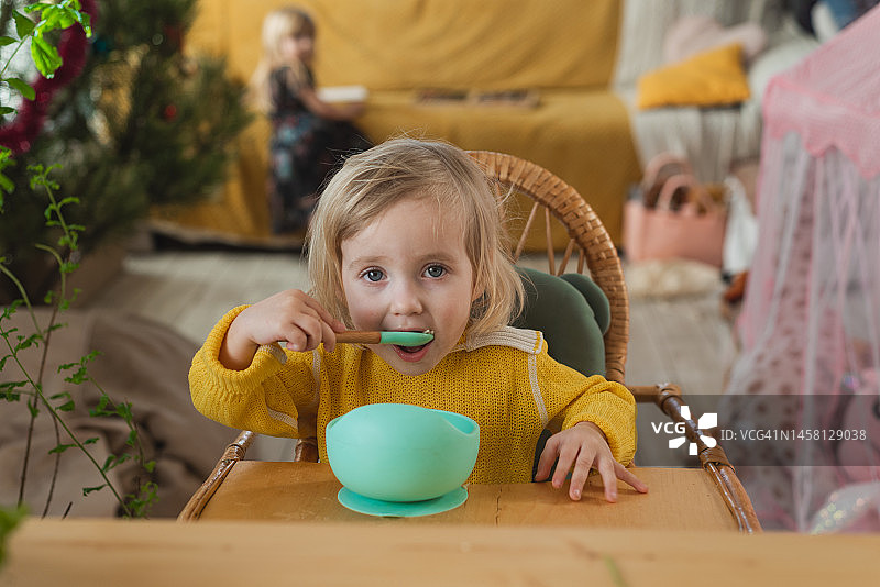 小女孩在家里的高脚椅上吃饭，独立儿童发育、合理营养和维生素概念图片素材