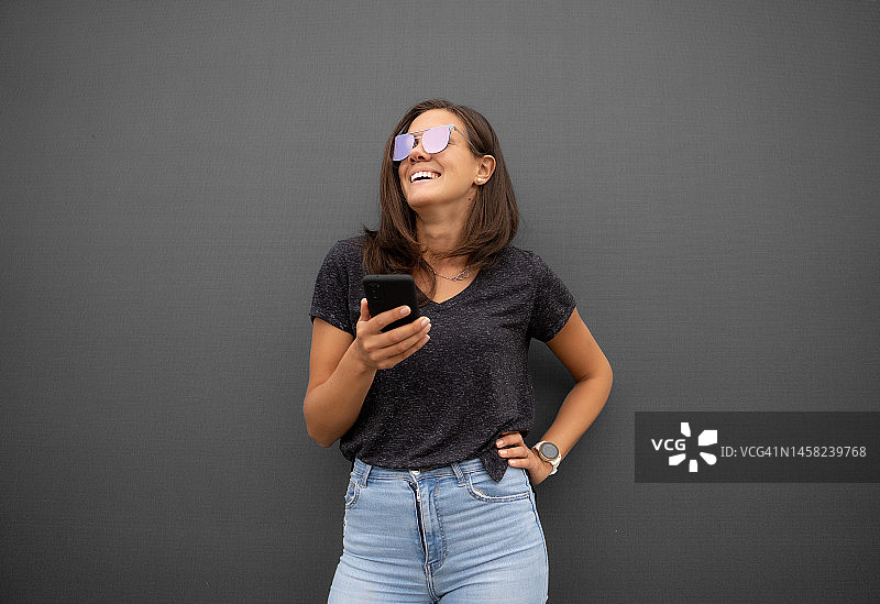 快乐的年轻女子在户外使用手机的肖像照，背景为纯灰色图片素材