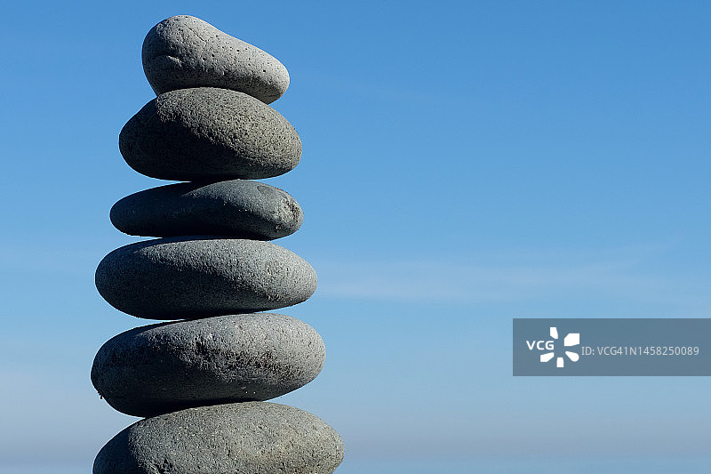 海边沙滩上用海石或大卵石堆成的金字塔，以蓝色天空和地平线为背景。灵魂和谐与平衡的概念图片素材
