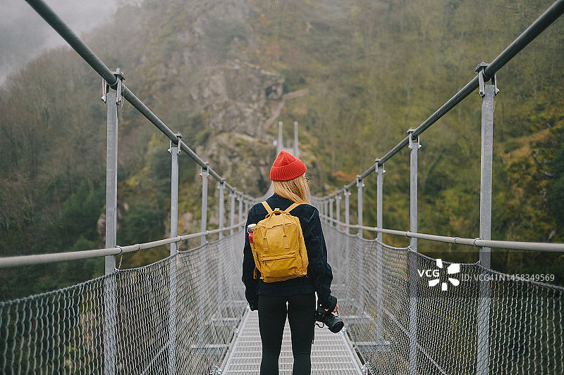 拿着相机的年轻女人在雾中穿过吊桥图片素材