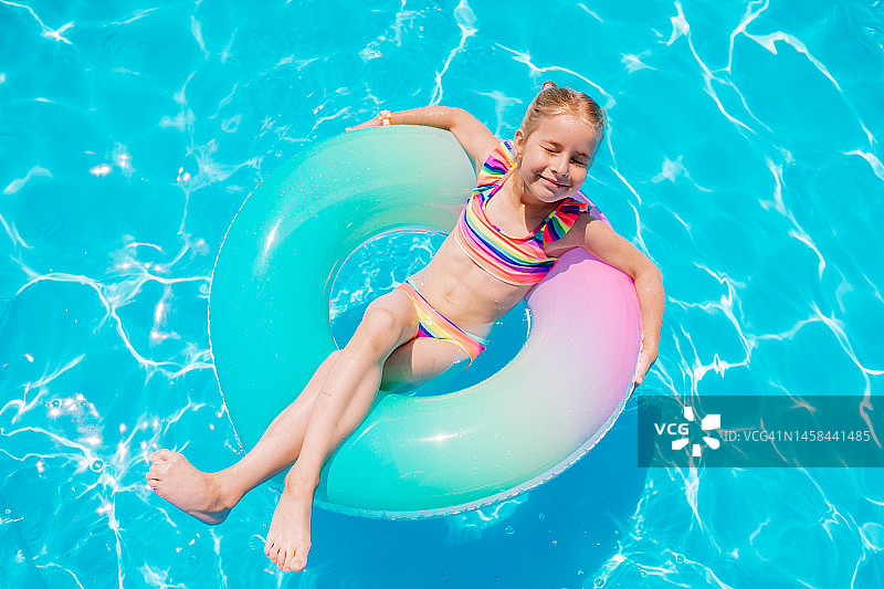 微笑的女孩在泳池的充气游泳圈上享受阳光图片素材