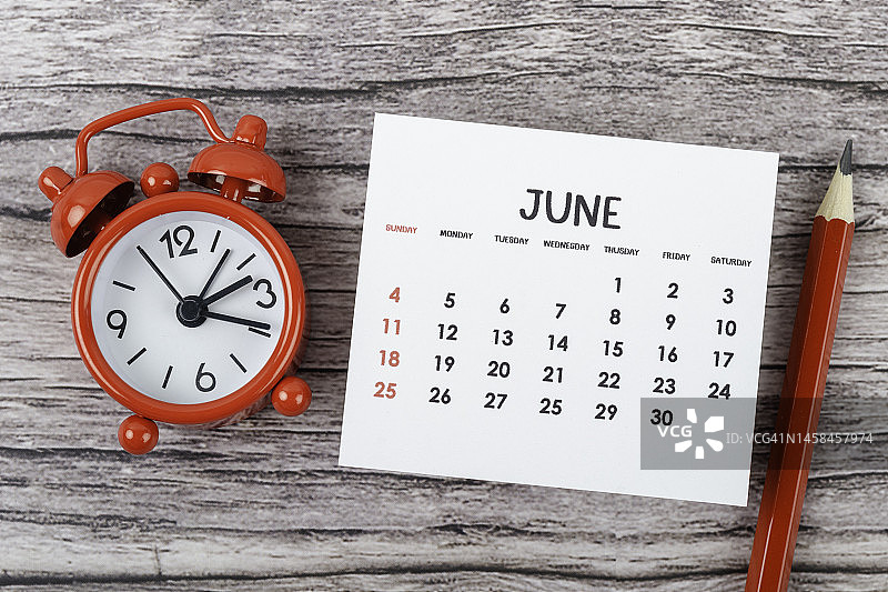 2023年台历：六月，带闹钟和红色铅笔的计划备忘，木桌背景图片素材