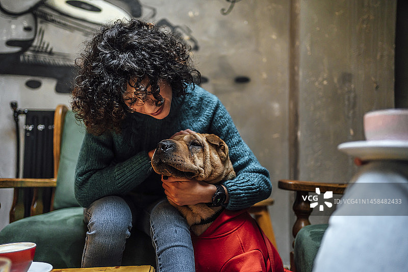 在咖啡馆里和她的狗一起玩耍的快乐女人图片素材