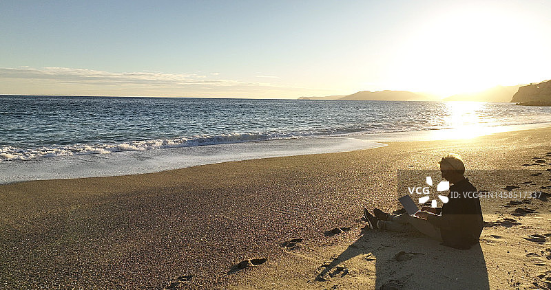 在沙滩上放松，使用手机的男子图片素材