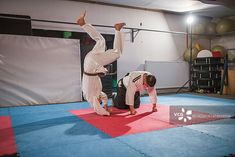 年轻的战士在健身房练习合气道摔法，并在他的合气道大师身上进行前翻练习图片素材