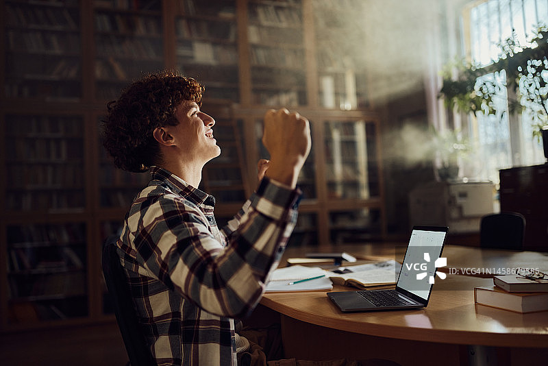 快乐的男学生在图书馆庆祝成功图片素材