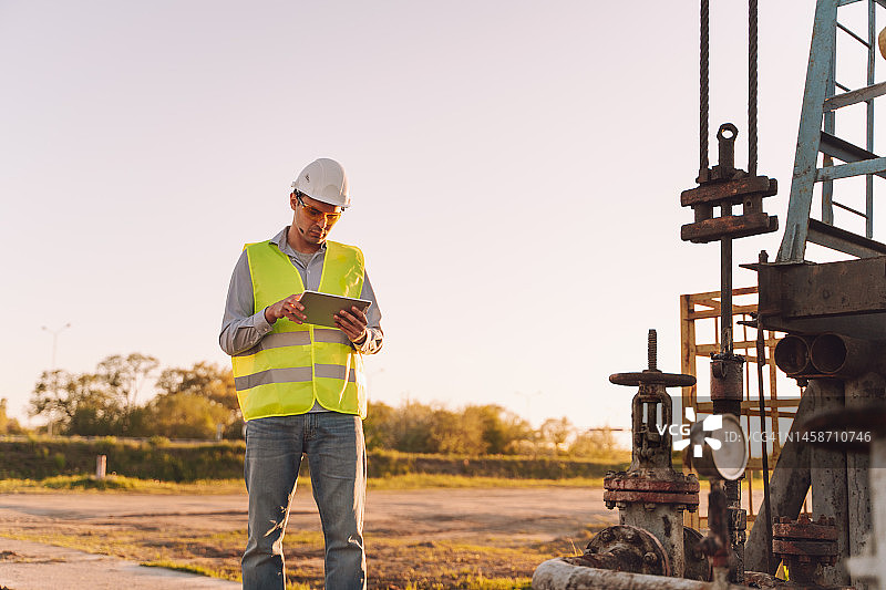 专业检验员在油气田油井泵附近测量和分析移动设备上的数据图片素材