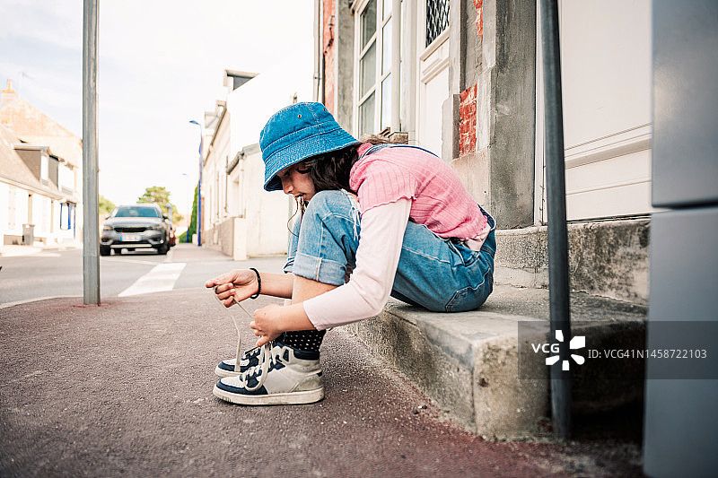 戴帽子的女孩坐在台阶上系鞋带图片素材