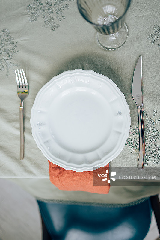 午餐的一切都准备好了:漂亮的桌子上有一个白色的盘子，叉子，刀，一个杯子和一张橙色的餐巾图片素材