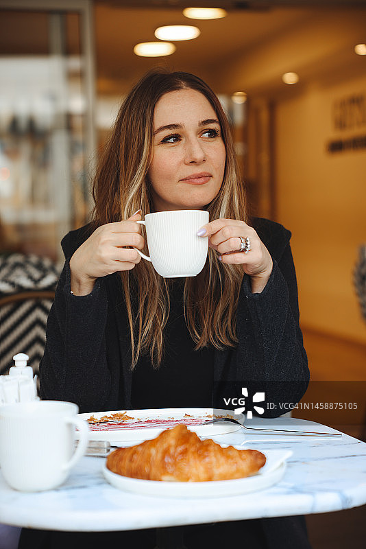咖啡馆里的卡布奇诺和法式羊角面包，一位女士正在享用早餐图片素材